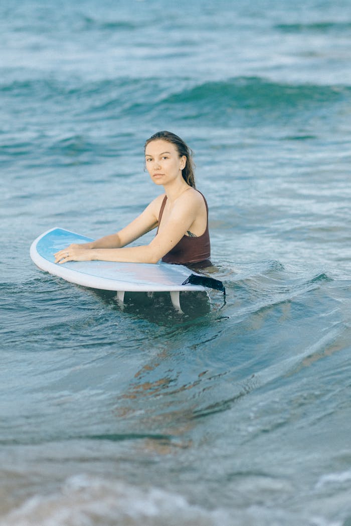 A woman with a surfboard enjoys a peaceful moment in the clear ocean waters.
