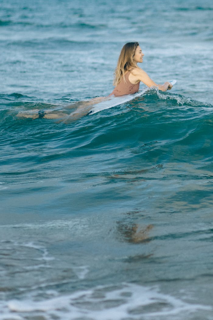 A woman paddles on a surfboard in the ocean, enjoying surfing in sunny weather.